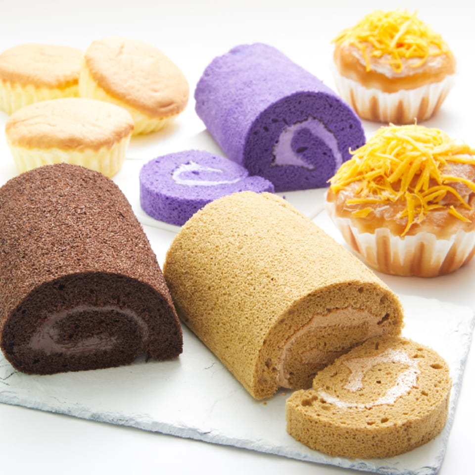 Assortment of Goldilocks Filipino bakery items: chocolate, ube, and mocha roll cakes, plus mamon and ensaymada.