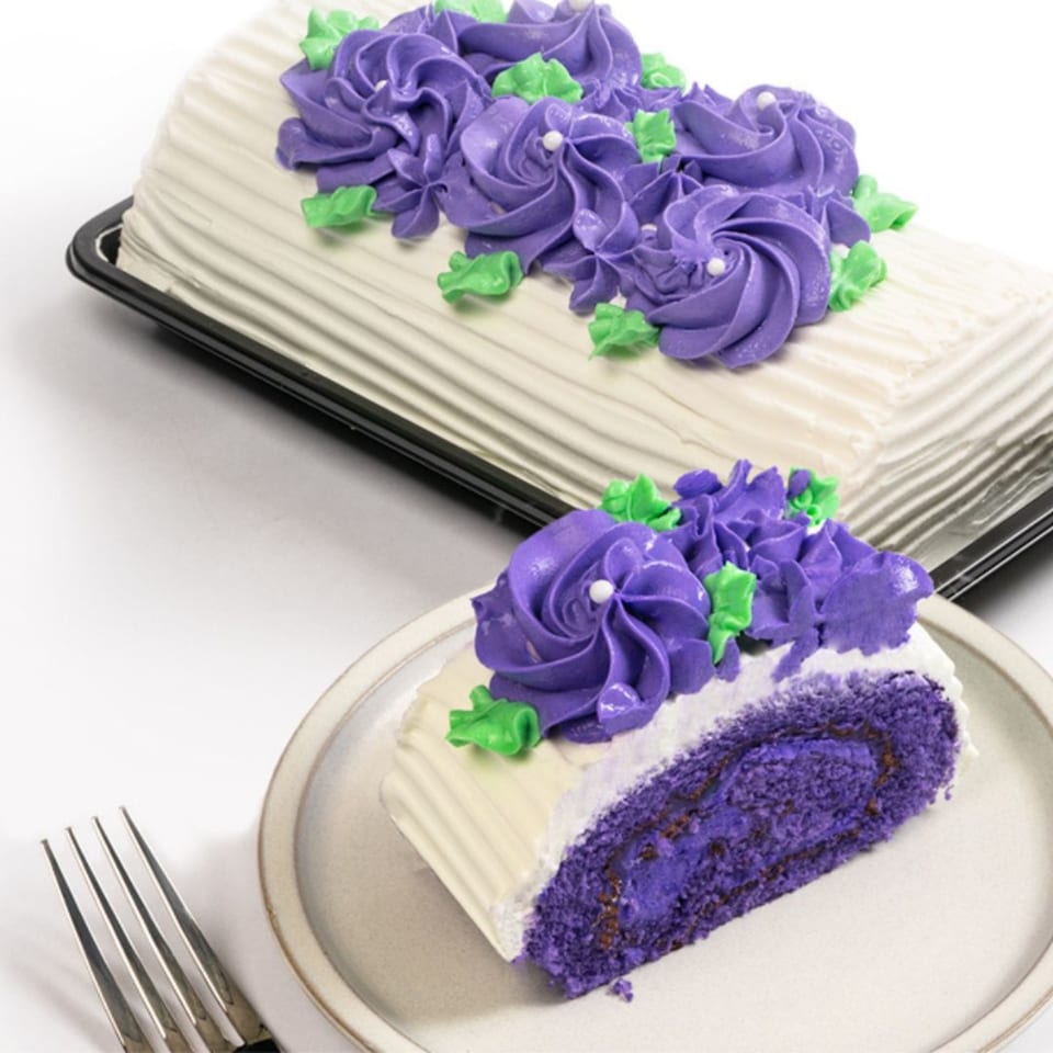 Ube log cake with purple frosting flowers and green leaves, with a slice on a plate.