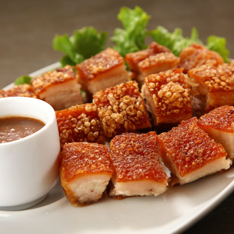 Crispy Filipino Lechon Kawali pork belly pieces with a side of dipping sauce and lettuce.