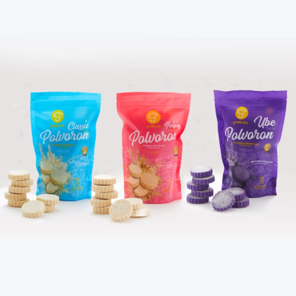 Three Goldilocks Polvoron bags: Classic, Pinipig, and Ube, with stacks of shortbread cookies.