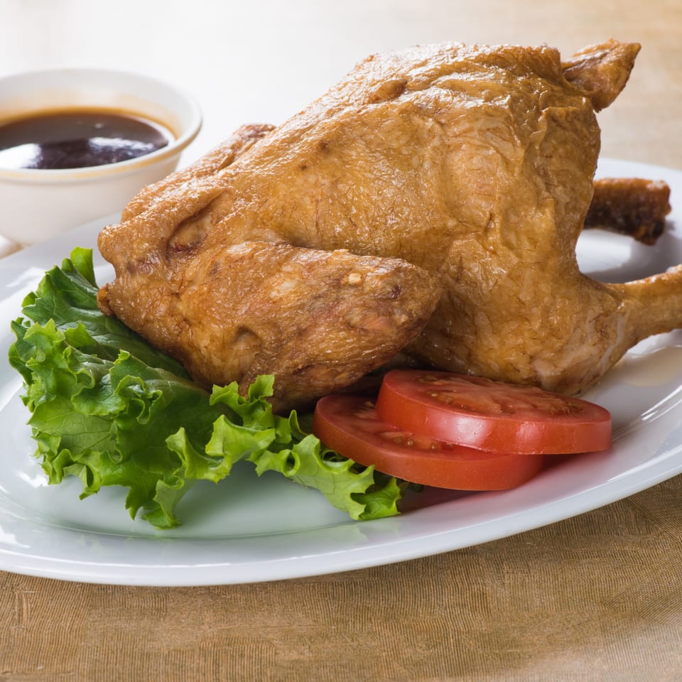 Whole fried chicken with lettuce, tomato slices, and a side of dark dipping sauce.