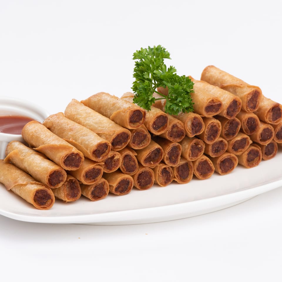 A white platter piled high with Goldilocks' crispy Filipino lumpia rolls, garnished with parsley and dipping sauce.