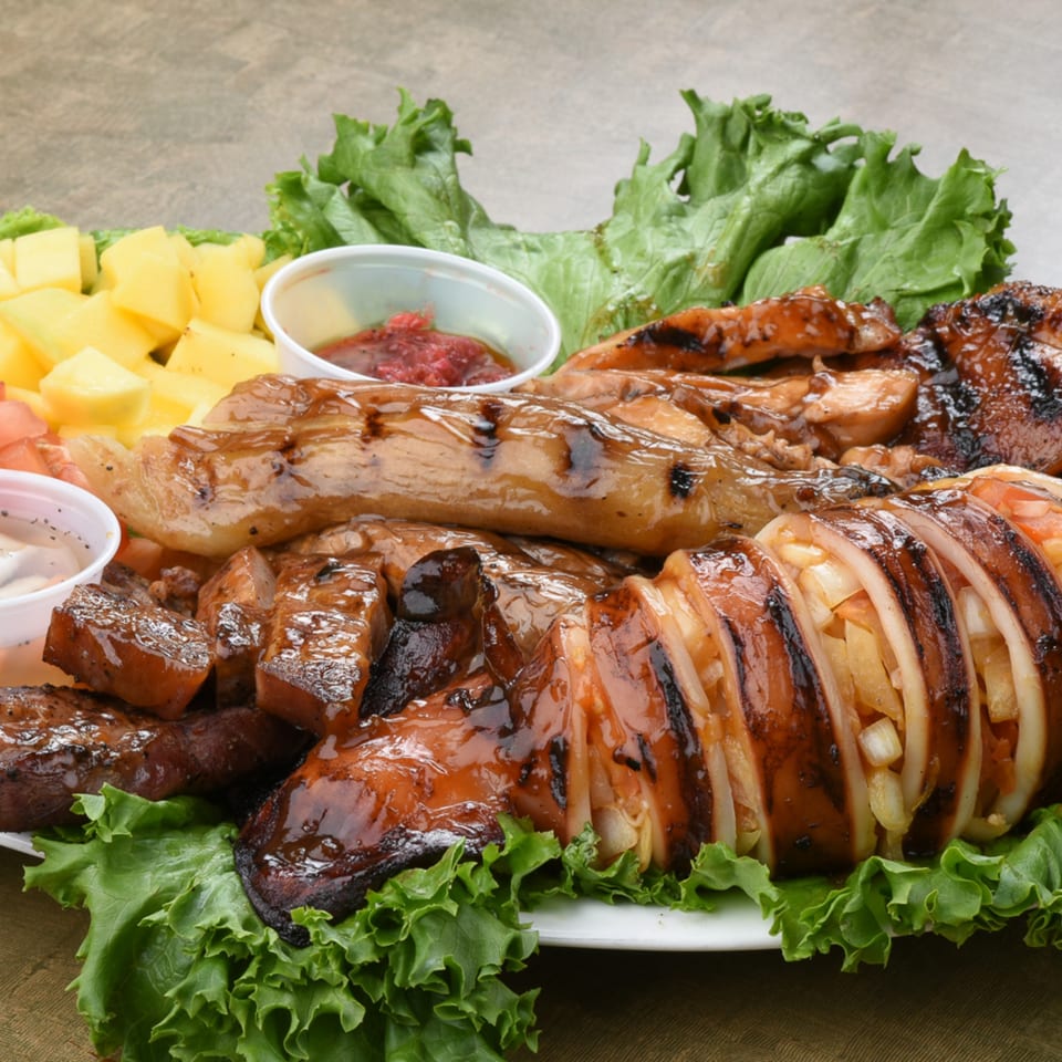 Grilled squid and various meats, with pineapple chunks, lettuce, and dipping sauces on a white plate.
